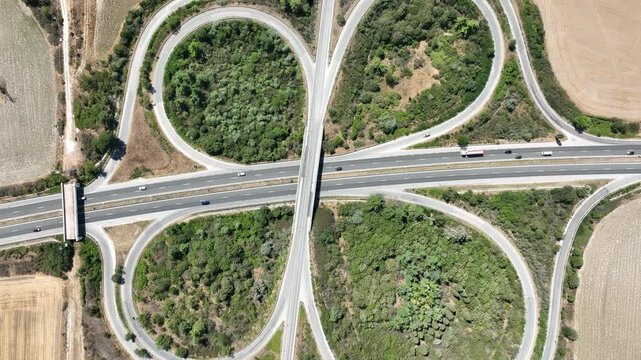 Aerial top down view of a symmetrical cloverleaf highway interchange. Cars on the road network show transportation and logistics in a rural landscape, symbolizing connectivity and infrastructure.