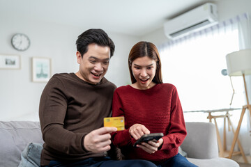 Asian couple using smartphone shopping online in living room at home