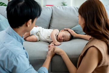 Obraz premium Asian parents looking at baby boy sleep on sofa in living room at home. 