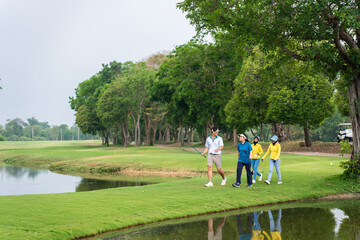 Professional young golfers walk with caddy cross lush green fairway. 