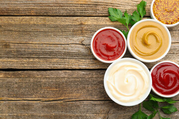 Different sauces in bowls and fresh parsley on wooden table, flat lay. Space for text