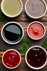 Different sauces in bowls with fresh dill on wooden table, flat lay