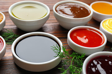 Different sauces in bowls with fresh dill on wooden table, closeup