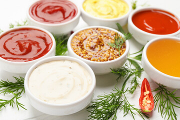 Different sauces in bowls and ingredients on white table, closeup
