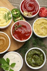 Different sauces and herbs on wooden table, flat lay