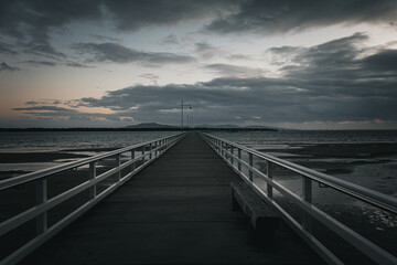Fototapeta premium The Port Welshpool Long Jetty in South Gippsland, Victoria, stretching into Corner Inlet under a dramatic, moody sky
