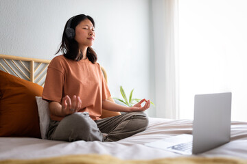 Woman meditating on bed with headphones and laptop