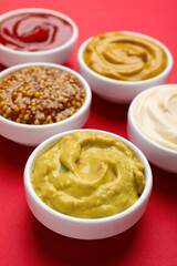 Different sauces in bowls on red background, closeup