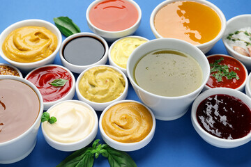 Different sauces and herbs on blue background, closeup