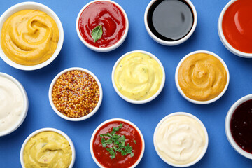 Different sauces and herbs on blue background, flat lay