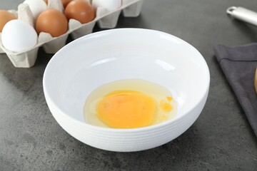 Bowl with broken egg on grey table, closeup