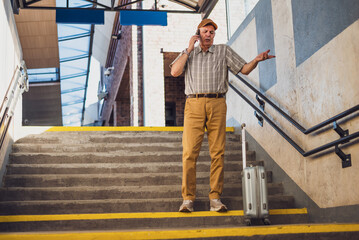 Senior man is standing at railway station and talking on mobile phone. He is distraught. Senior people traveling.