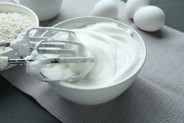 Whipped whites in bowl, mixer, flour and eggs on grey wooden table, closeup