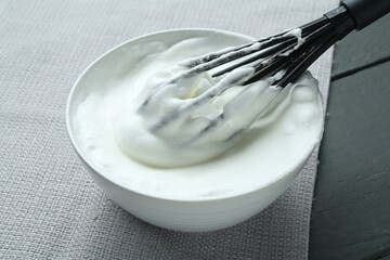 Whipped whites in bowl, whisk and eggs on grey wooden table, closeup
