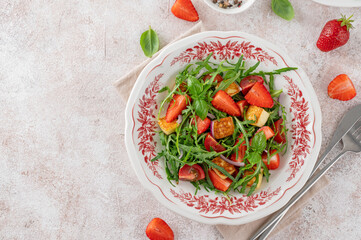 Healthy salad with strawberries, tomatoes, arugula, halloumi cheese and basil on a plate on a concrete background. Top view, copy space.
