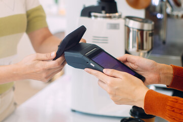 Asian woman paying for purchase with mobile phone at coffee shop. Contactless payment at cafe restaurant. Customer using NFC Smartphone making payment, paying on terminal. Cashless payment technology.