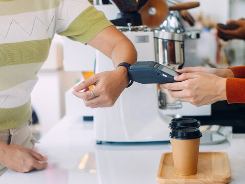 Close-up of woman hand using smartwatch tapping on terminal for contactless payment, checkout, making a payment at coffee shop. Customer making wireless, cashless payment using smart watch.