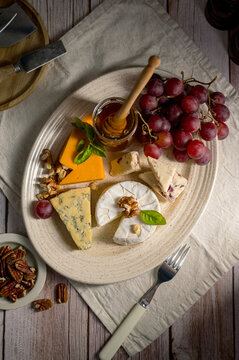 Assorted cheese plate with grapes honey and nuts on rustic wooden table