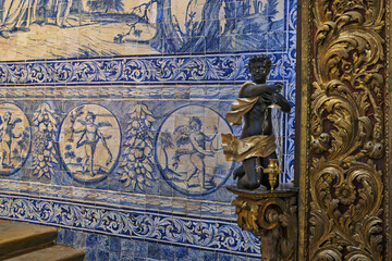 Statue of a dark cherub holding a golden incense burner,set against a blue and white tile mural depicting classical scenes in Faro cathedral, Portugal
