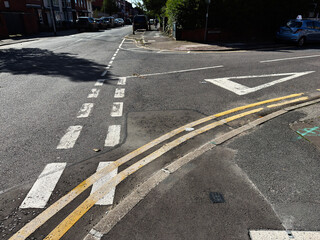 Busy Manchester street intersection with faded road markings, curbs, and parked cars in sunlight