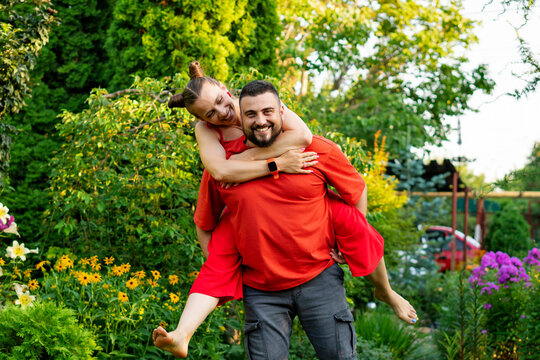 Couple enjoying playful piggyback ride in vibrant garden - Powered by Adobe