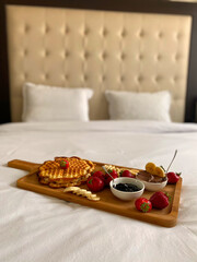 Fresh breakfast with waffles and berries served on a bed in a hotel room