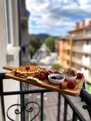 Waffles and fruit breakfast served on a balcony with city view