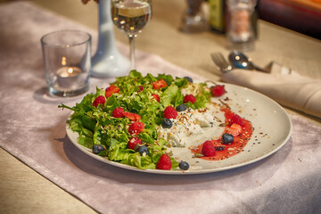 Fresh green salad with berries and cream cheese on elegant restaurant table