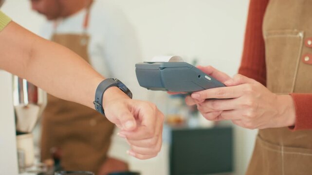 Close-up of woman hand using smartwatch tapping on terminal for contactless payment, checkout, making a payment at coffee shop. Customer making wireless, cashless payment using smart watch.