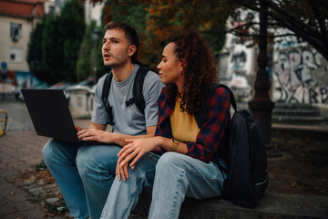 Students using laptop and discussing outdoors in urban setting