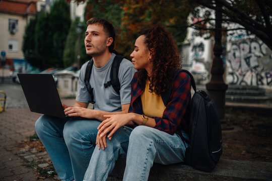 Students using laptop and discussing outdoors in urban setting