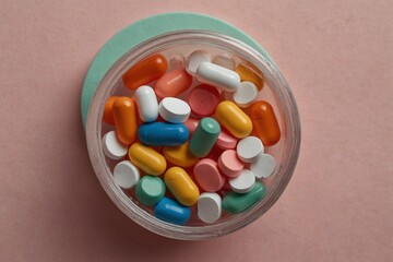 Assorted colorful pills in round container on pink background