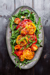 Organic Heirloom Tomato salad with salt and arugula on black wooden background top view