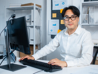 Portrait of Professional Confident Asian Business manager looking at camera with Smiling face sit at desk in office while working on desktop computer. headshot of Asian businessman looking at camera.