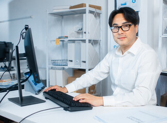 Portrait of Professional Confident Asian Business manager looking at camera with Smiling face sit at desk in office while working on desktop computer. headshot of Asian businessman looking at camera.