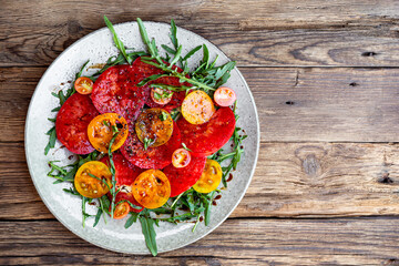 Organic Heirloom Tomato salad with salt and arugula on wooden background top view copy space for text