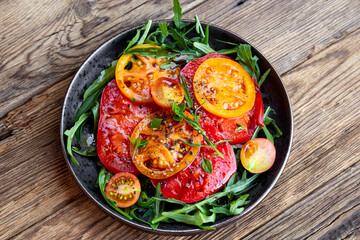 Organic Heirloom Tomato salad in a plate with salt and arugula on wooden background top view