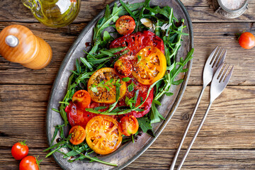 Organic Heirloom Tomato salad with salt and arugula on wooden background top view