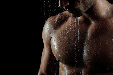 Muscular man under shower with water droplets on his skin against black background