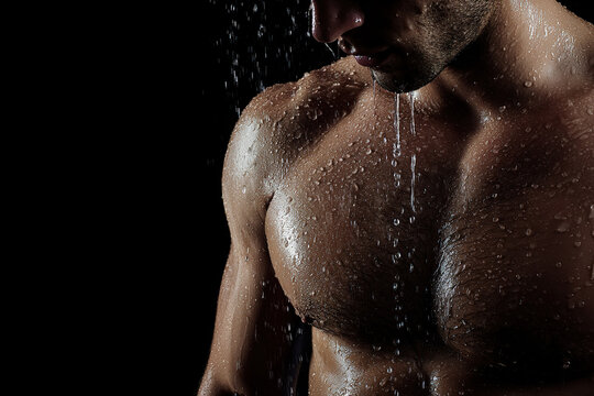 Muscular man under shower with water droplets on his skin against black background