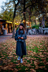 Stylish middle-aged woman wearing long coat and knitted beanie and using smartphone outdoors