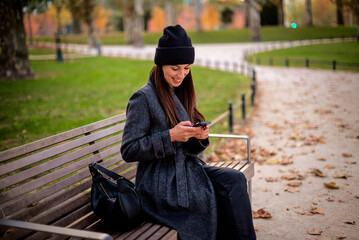 Confident smiling woman sitting at the city park and using a smartphone