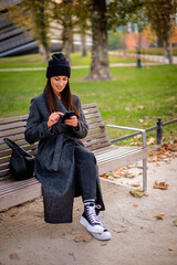 Confident smiling woman sitting at the city park and using a smartphone