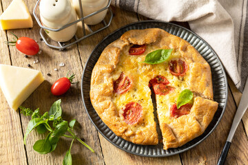 Crispy tomato galette with adyghe cheese and herbs on rustic background.