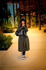 Confident and attractive woman wearing warm knitted scarf and beanie while standing in the park in an autumn day
