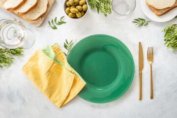 Festive table setting with empty plate, cutlery and napkin - green leaves decorated, bread and olives for dinner, flat lay. Top view