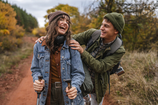 Young couple hiking trail, sharing laughter in autumn forest