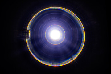 a circular light source with a bright white center, surrounded by concentric rings of rainbow light. The light rings appear slightly blurred, giving a dynamic, almost swirling effect