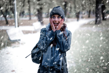 Cheerful smiling woman standing in the snowfall at the park