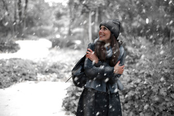 Cheerful smiling woman standing in the snowfall at the park
